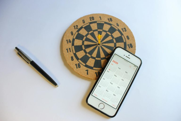 A smartphone with a 2020 calendar next to a dartboard and pen on a white surface.