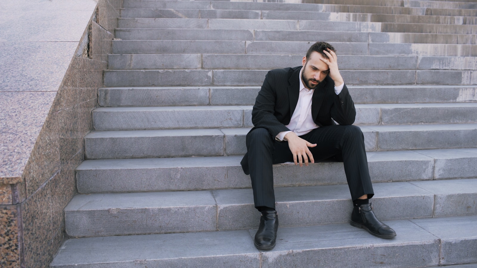 Man in suit sitting on steps, head in hand.
