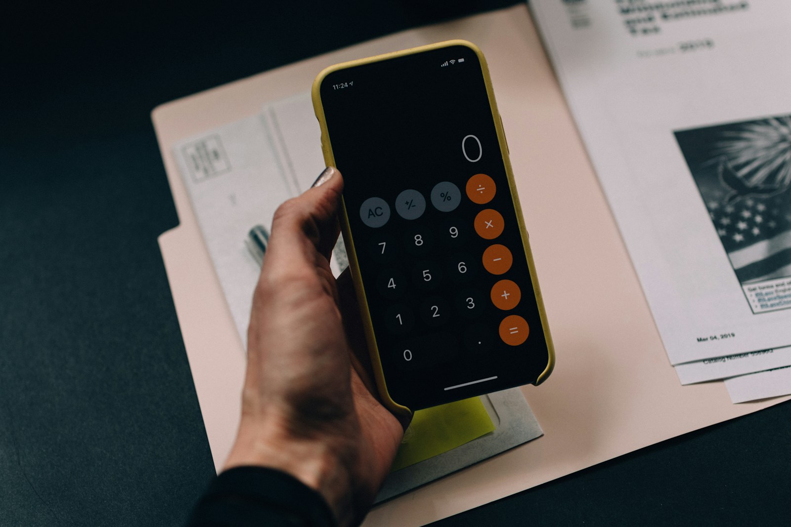 A hand holding a smartphone displaying a calculator app over a paper folder